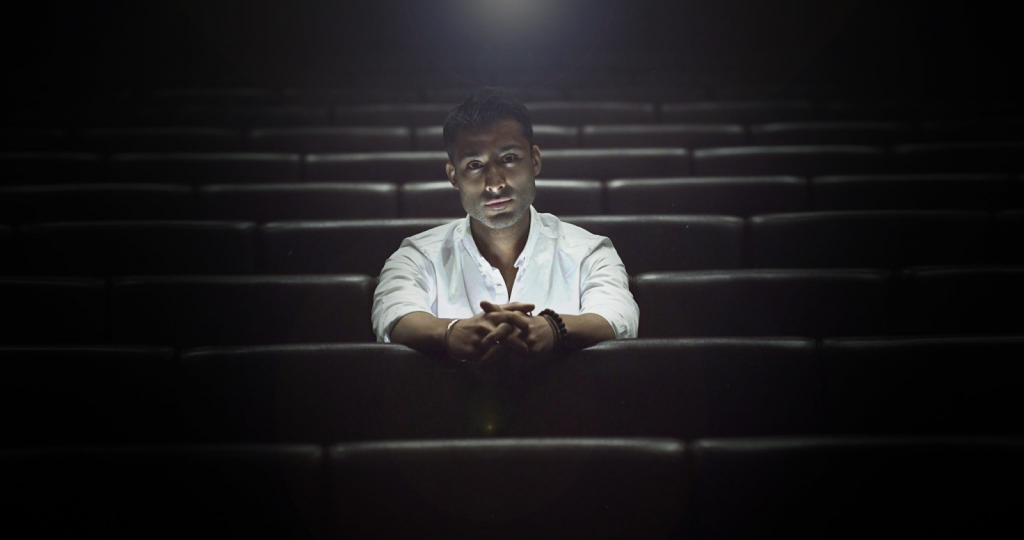 A picture of Jay Cruiz sitting in a dimly lit movie theater, facing the camera.