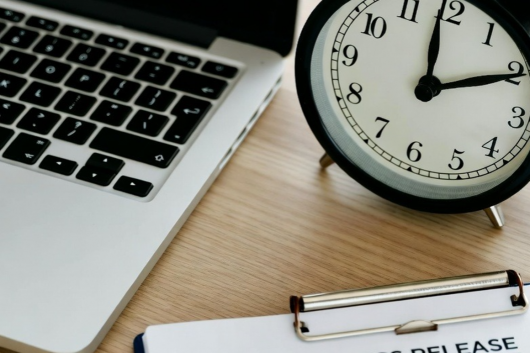 Clock on desk next to laptop with calendar showing optimal press release timing schedule