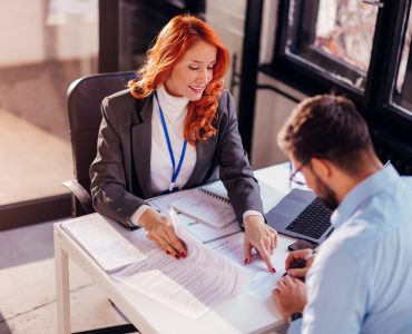 Two business professionals discussing contract terms at an office desk